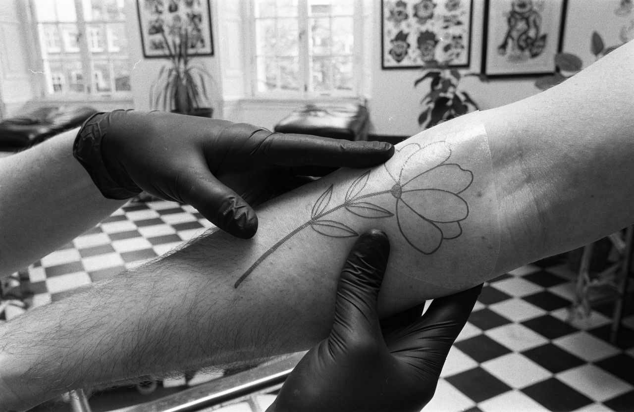 An artist in black gloves pressing a flower stencil onto a forearm